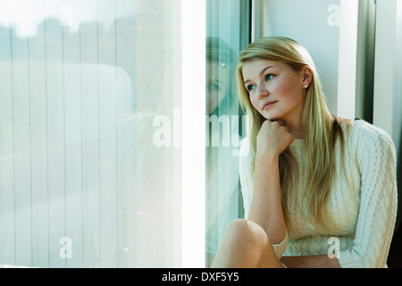 Giovane donna a guardare fuori dalla finestra, Mannehim, Baden-Württemberg, Germania Foto Stock