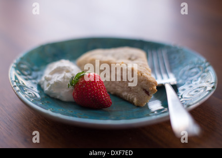 Freschi di forno scone con panna montata e una fragola su una piastra blu con una forcella Foto Stock