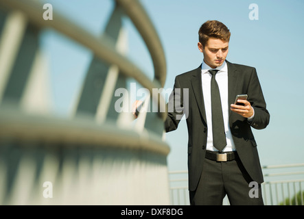 Ritratto di imprenditore in piedi dalla ringhiera e guardando lo smartphone, Germania Foto Stock