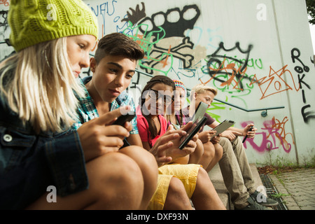 Un gruppo di bambini seduti sulle scale all'aperto, utilizzando i computer tablet e smartphone, Germania Foto Stock