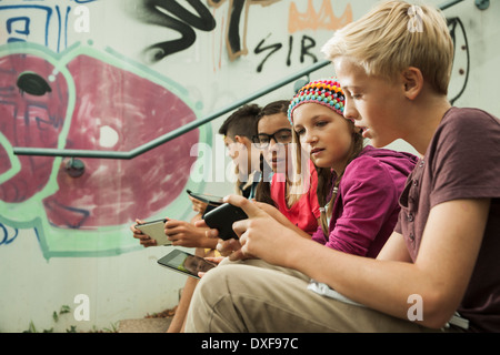 Un gruppo di bambini seduti sulle scale all'aperto, utilizzando i computer tablet e smartphone, Germania Foto Stock