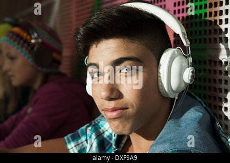 Close-up ritratto di ragazzo seduto accanto alla parete esterni, indossa le cuffie e guardando la telecamera, Germania Foto Stock