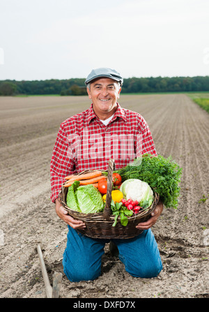 Ritratto di agricoltore in ginocchio in campo, cestello di contenimento di verdure fresche, sorridente e guardando la telecamera, Hesse, Germania Foto Stock
