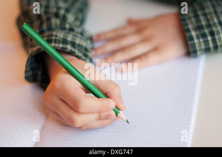 Bambino la scrittura a mano su un foglio di carta con la matita verde Foto Stock