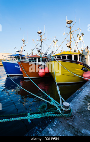 Tre vivacemente colorato trawler barche da pesca legati assieme su un pontone in un porto. Foto Stock