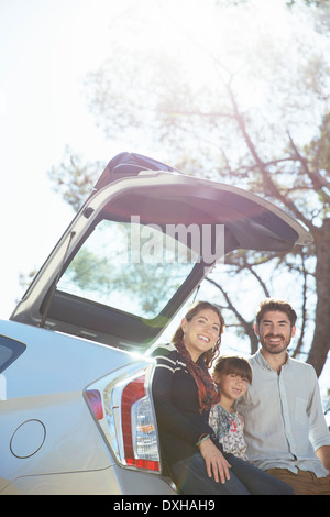 Ritratto di famiglia sorridente seduto contro la parte posteriore della macchina Foto Stock