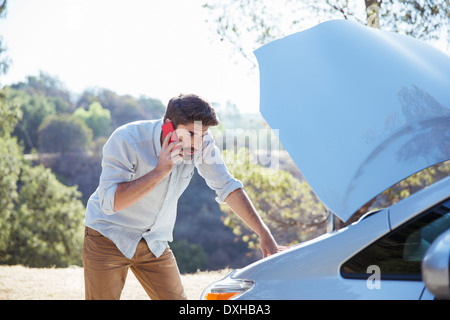 L'uomo parlando al cellulare e controllo motore auto in strada Foto Stock