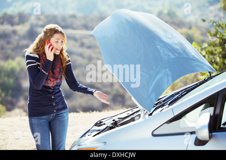 Frustrati donna parlando al cellulare con automobile cofano sollevato in banchina Foto Stock