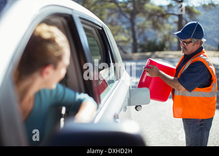 La donna guarda la strada meccanico di riempimento del serbatoio del gas Foto Stock