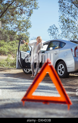 Donna che parla al cellulare in strada dietro il triangolo di avvertenza Foto Stock