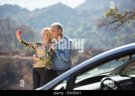 Coppia senior tenendo Self-portrait in strada fuori dall'auto Foto Stock