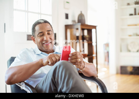 Uomo Senior per la messaggistica di testo con il cellulare in salotto Foto Stock