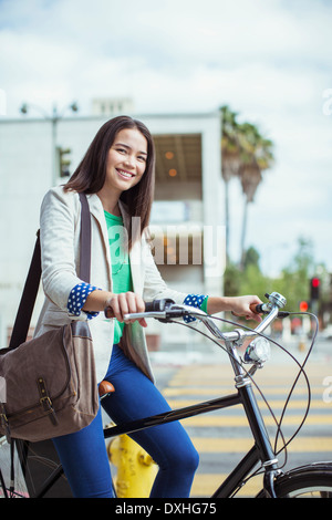 Ritratto di sorridente imprenditrice informale sulla bicicletta su strada urbana Foto Stock