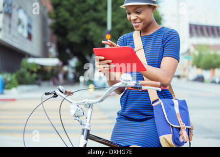 Casual imprenditrice utilizzando digitale compressa in bicicletta sulla strada urbana Foto Stock