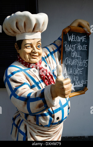 Un modello gigante chef maschio con chef tradizionale''s hat e abbigliamento winking e mostrando pollice in alto tenendo premuto menu, REGNO UNITO Foto Stock