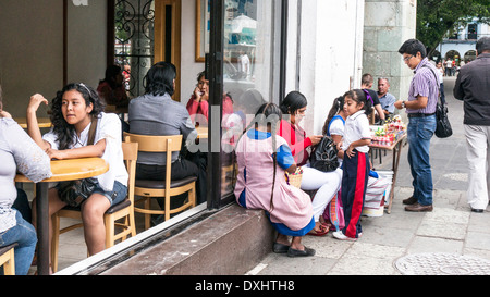 Ignorato da patroni all'interno cafe ben vestiti Donna con bambina si siede sul davanzale della finestra aperta tra 2 fornitori indigeni Foto Stock