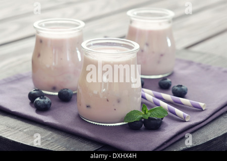Yogurt con maturi ai mirtilli freschi in vasi su sfondo di legno Foto Stock
