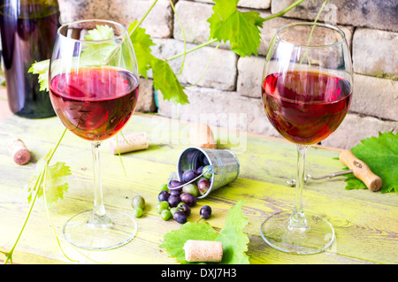 Due bicchieri di vino rosso sullo sfondo di un vecchio muro di mattoni e di vigneti. Dietro ad una benna di acini di uva Foto Stock