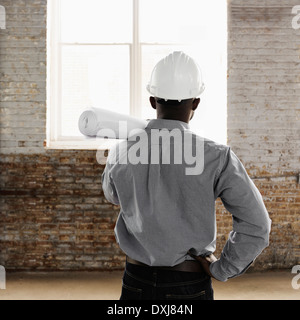 Architetto nero indossando hard-hat e azienda blueprints Foto Stock