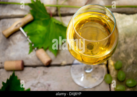 Bicchiere di vino bianco nella parte superiore dello sfondo di pietra, cavatappi e sughero, foglie di vite e uva. Foto Stock