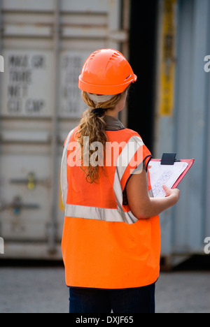 Lavoratore di sesso femminile che negli appunti con il controllo di contenitori in container terminal vista posteriore Foto Stock