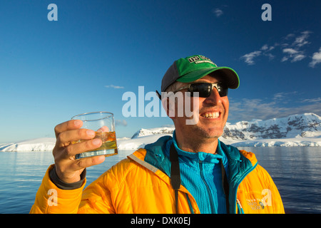 Un passeggero in possesso di un Scotch sulle rocce con centomila anni di ghiaccio del ghiacciaio nel suo drink, sul ponte della Akademik Sergey Vavilov, un rafforzamento del ghiaccio nave per una crociera spedizione in Antartide, fuori della penisola antartica a stretto di Gerlache. La penisola antartica è uno dei più rapidamente il riscaldamento luoghi sul pianeta. Foto Stock