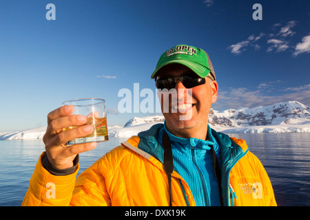 Un passeggero in possesso di un Scotch sulle rocce con centomila anni di ghiaccio del ghiacciaio nel suo drink, sul ponte della Akademik Sergey Vavilov, un rafforzamento del ghiaccio nave per una crociera spedizione in Antartide, fuori della penisola antartica a stretto di Gerlache. La penisola antartica è uno dei più rapidamente il riscaldamento luoghi sul pianeta. Foto Stock