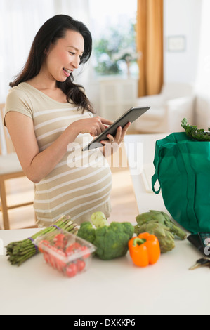 Incinta donna giapponese con tavoletta digitale in cucina Foto Stock