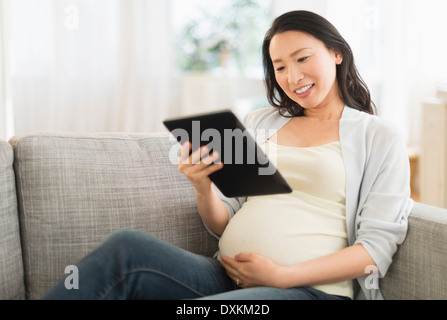 Incinta donna giapponese con tavoletta digitale sul divano Foto Stock