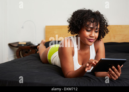 Razza mista donna utilizzando digitale compressa sul letto Foto Stock