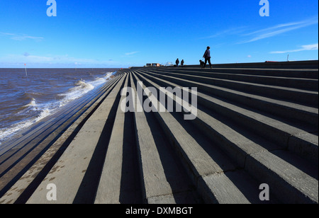 Walkers lungo la parte superiore della parete del mare ad alta marea a Heacham sulla costa di Norfolk. Foto Stock