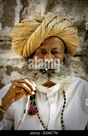 Anziani grigio-uomo barbuto con turbante giallo di fumare un narghilè in Forte Mehrangarh di Jodhpur, India. Manipolati digitalmente immagine. Foto Stock