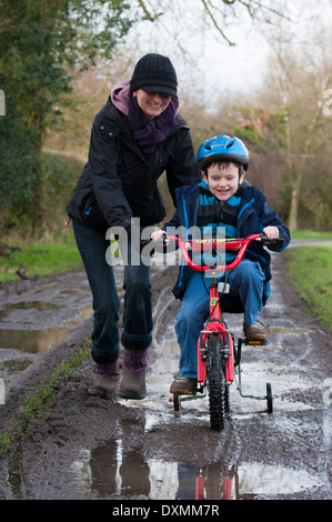 Madre figlio di spinta sulla bici su terreni fangosi via Foto Stock