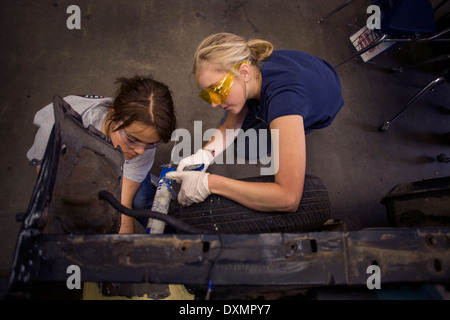 Indossare occhiali di sicurezza due ragazze adolescenti a lavorare insieme su un auto in auto shop classe in San Clemente, CA. Foto Stock