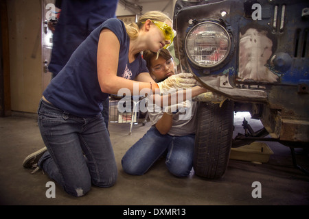 Indossare occhiali di sicurezza due ragazze adolescenti a lavorare insieme su un auto in auto shop classe in San Clemente, CA. Foto Stock