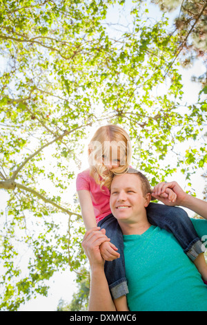 Carino ragazza giovane corse Piggyback sul suo papà le spalle al di fuori del parco. Foto Stock