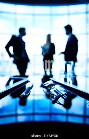 Immagine di occhiali, touchpad e penna in luogo di lavoro con un gruppo di imprenditori la comunicazione sullo sfondo Foto Stock