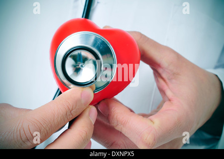 Un medico auscultating un cuore rosso con uno stetoscopio Foto Stock