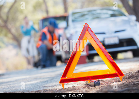 Il triangolo di avvertenza sulla strada con meccanico in background Foto Stock