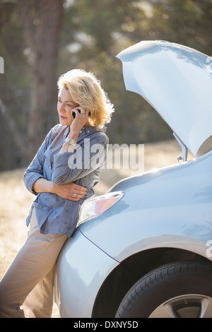 Donna che parla al cellulare con automobile cofano sollevato in banchina Foto Stock