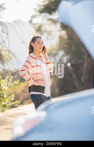 Donna che parla al cellulare con automobile cofano sollevato in banchina Foto Stock
