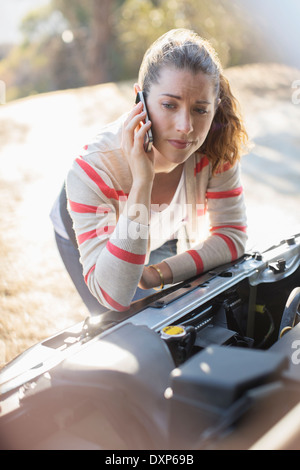 Frustrati donna parlando al cellulare e guardando il motore per auto Foto Stock