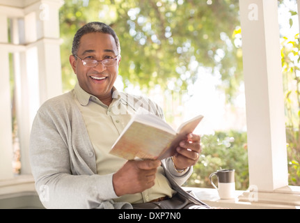 Ritratto di sorridente uomo senior leggendo un libro sul portico Foto Stock