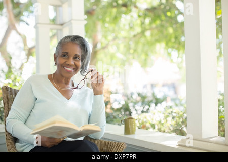 Ritratto di sorridente donna senior leggendo un libro sul portico Foto Stock