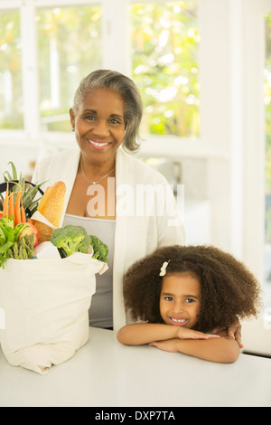 Ritratto di nonna sorridente e nipote con negozi di generi alimentari in cucina Foto Stock