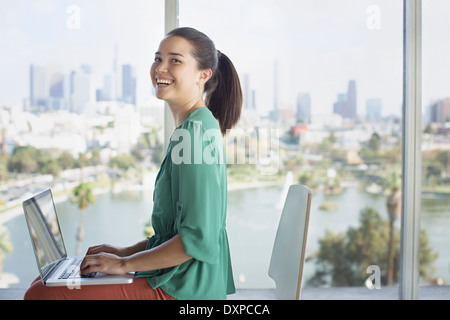 Ritratto di fiducioso casual imprenditrice a laptop vicino alla finestra vista città Foto Stock