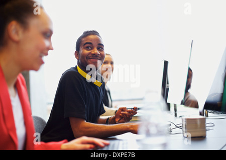 Giovani afro-americano di uomo che guarda lontano sorridere mentre in laboratorio informatico. Giovani studenti seduti a tavola con i computer. Foto Stock