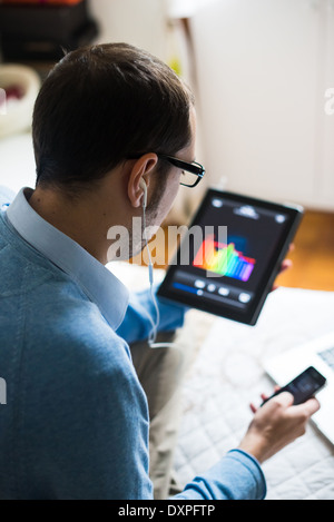 Elegante business multitasking uomo multimediale utilizzando dispositivi a casa Foto Stock
