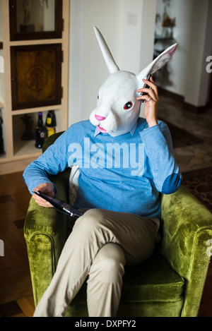 Elegante business multitasking maschera di coniglio uomo utilizzando dispositivi a casa Foto Stock