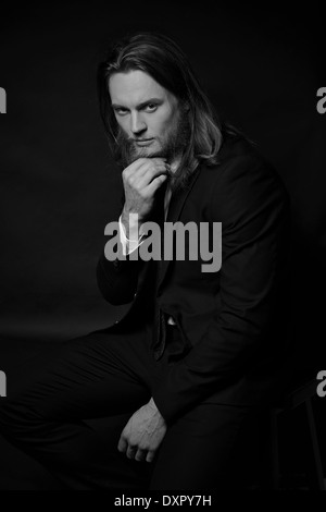 Un uomo in perline, capelli lunghi, modello maschile, in posa di un abito nero. Un buio in bianco e nero la moda maschile ritratto Foto Stock